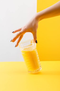 Gri ve sarı arka planda taze, lezzetli sarı smoothie bardağı tutan bir kadın görüntüsü.