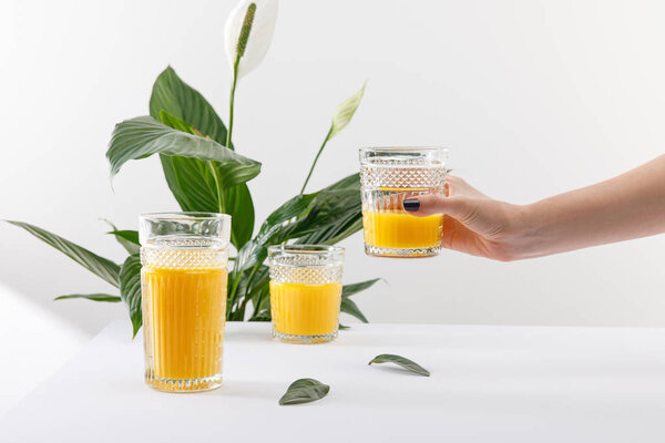 cropped view of woman holding glass of fresh delicious yellow smoothie near green peace lily plant on white background