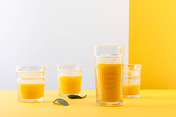 glasses of fresh delicious yellow smoothie near green leaves