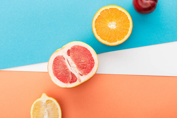 Top view of fruits halves and apple on blue, orange and white background