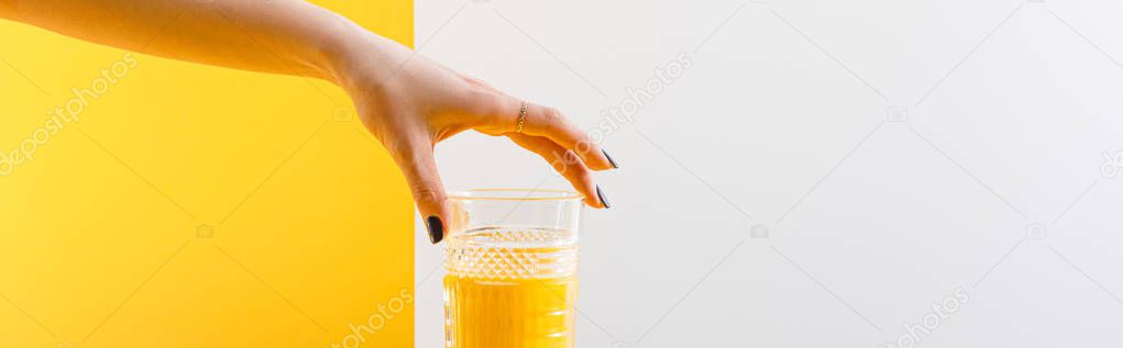 cropped view of woman holding glass of fresh delicious yellow smoothie on grey and yellow background, panoramic shot