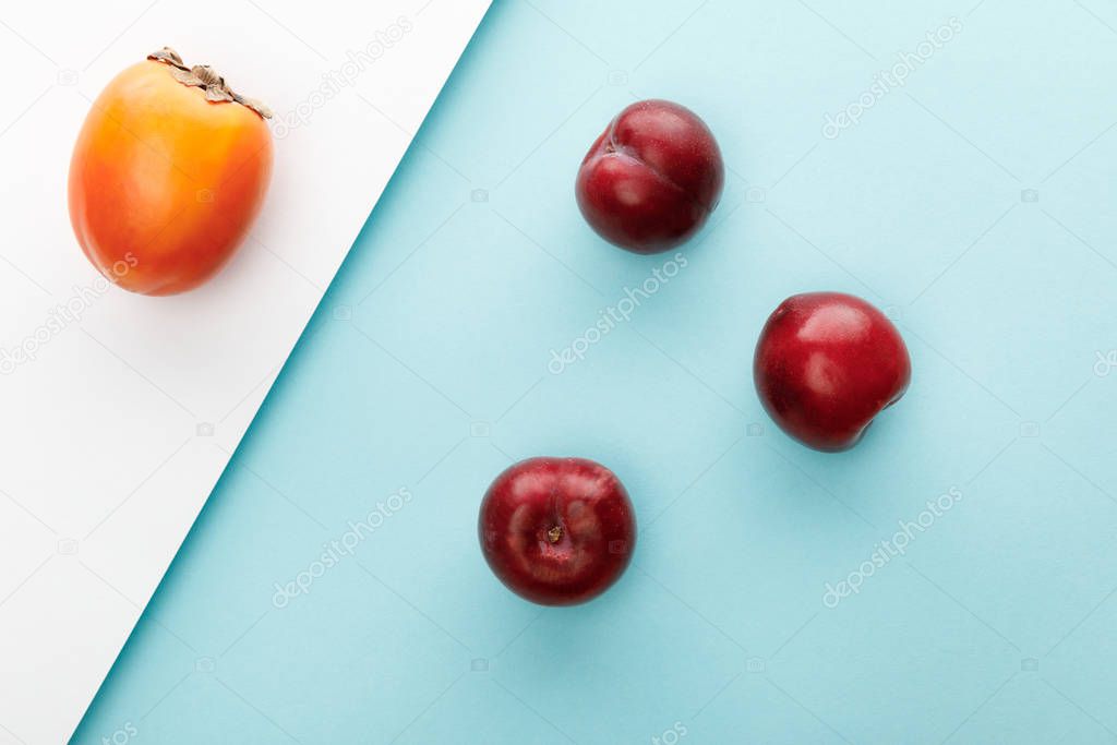 Top view of persimmon and apples on white and blue background
