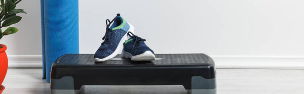 panoramic shot of step platform, blue fitness mat and sneakers at home 