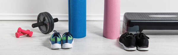 panoramic shot of yoga mats, sneakers, step platform and sport equipment on floor at home 