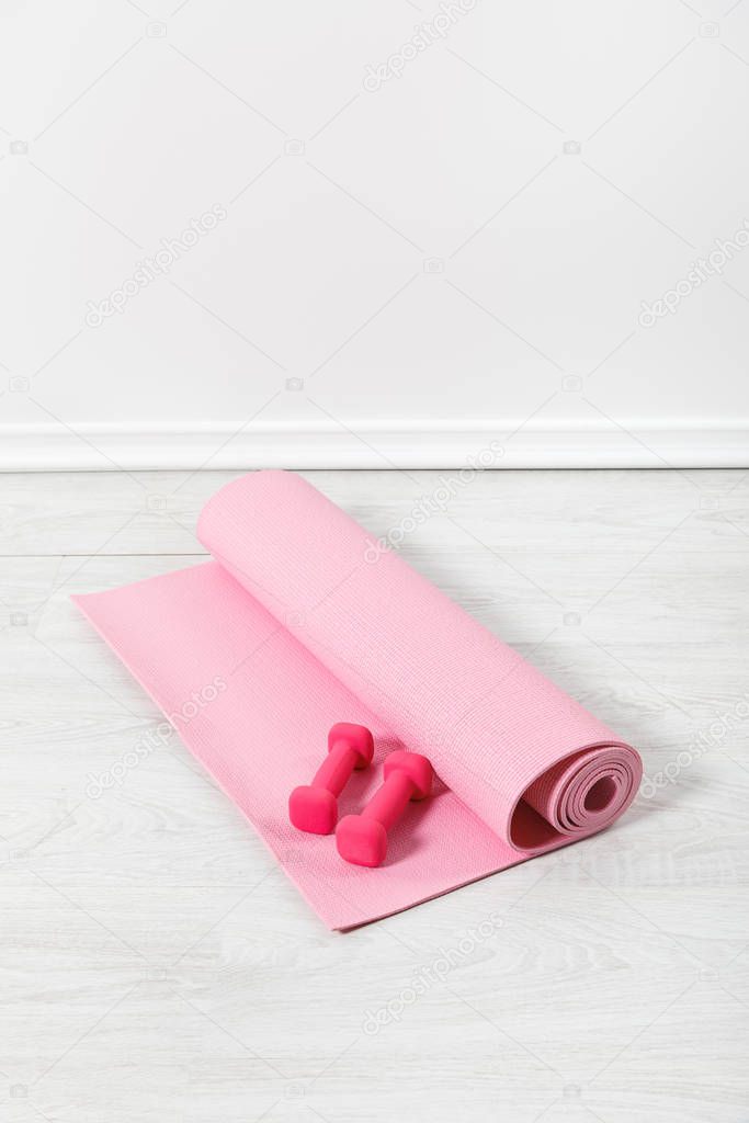 pink fitness mat and dumbbells on white floor