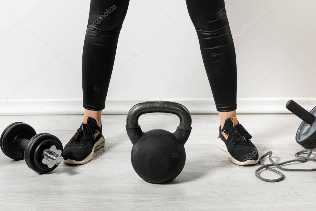 cropped view of athletic girl with kettlebell and sports stuff standing at home 