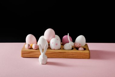 Süslü beyaz tavşanlar ve paskalya yumurtaları pembe ve siyah arka planda tahta tahtada.