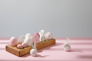Tahta üzerinde Paskalya yumurtaları ve pembe ve gri arka planda dekoratif tavşanlar.
