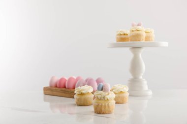 Selective focus of delicious Easter cupcakes on surface and cake stand and painted chicken eggs on grey background  clipart