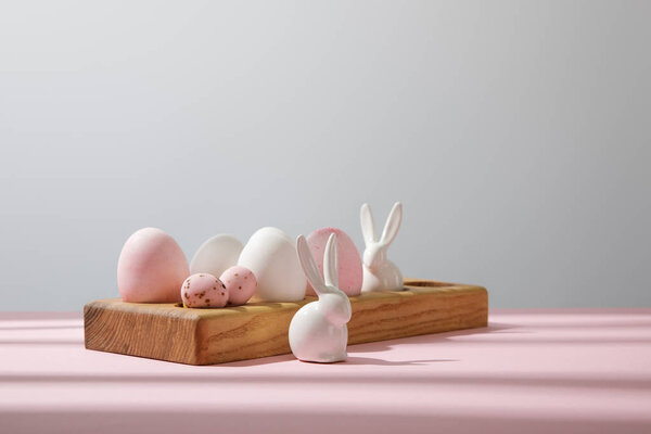 Easter eggs on wooden board with decorative rabbits on pink and grey