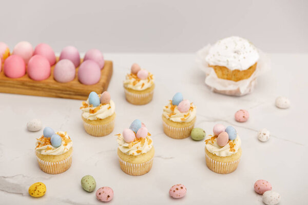 Cupcakes with painted chicken and quail eggs near traditional easter cake isolated on grey background