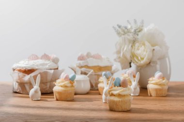 Dekoratif tavşanlı kekler, şeker kasesi, paskalya pastası ve gri renkli çiçekli vazolar.