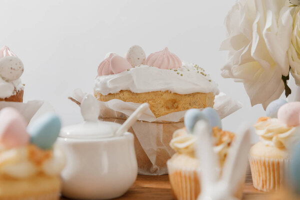 Selective focus of cupcakes, sugar bowl, Easter bread and flowers isolated on grey