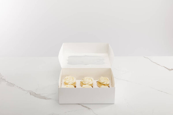 Tasty cupcakes in box isolated on grey