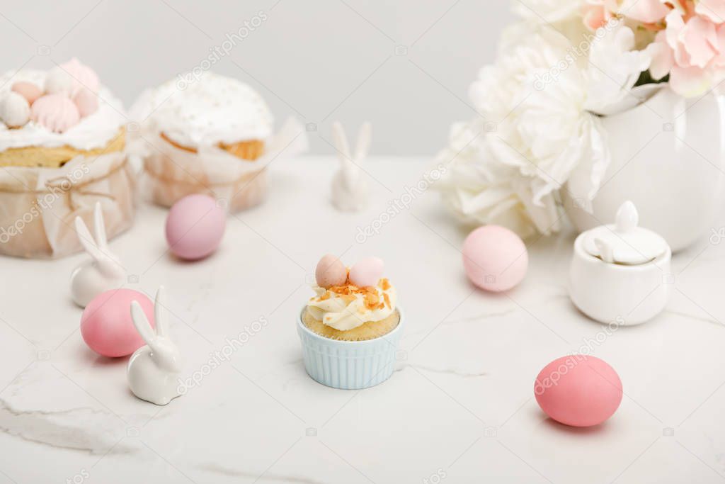 Selective focus of cupcake with colorful chicken eggs, decorative bunnies, sugar bowl, easter cakes and flowers isolated on grey