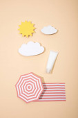 Horní pohled na papír řezané slunce, mraky, plážový deštník a deštník s tubou opalovacího krému na béžové
