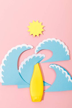 Kağıdın üst görüntüsü, pembe arka planda güneş ve deniz dalgalarını güneş kremiyle keser.