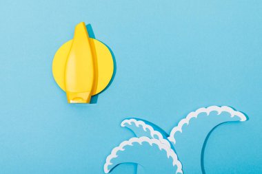 Güneş ve deniz dalgalarını mavi üzerine güneş kremi ile kesen kağıdın üst görüntüsü 