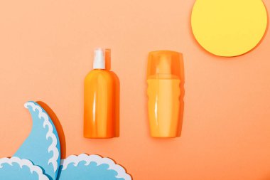 Top view of dispenser bottles of sunscreen with paper cut sun and sea waves on orange background clipart