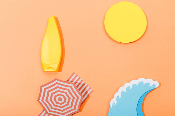 Top view of paper cut beach with tube of sunscreen on orange