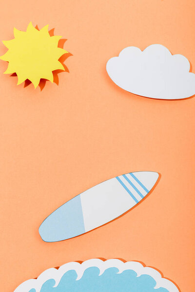 Top view of paper cut sun, cloud, surfboard and sea wave on orange background