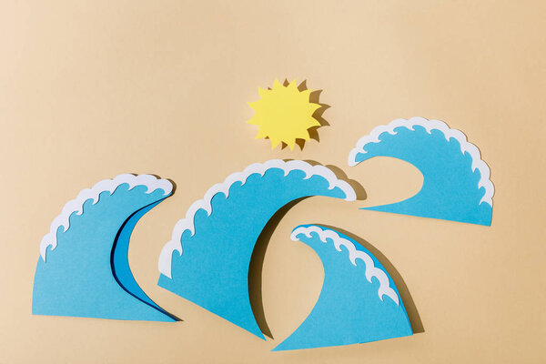 Top view of paper cut sun and sea waves on beige 