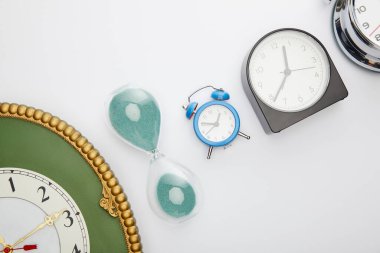 Beyaz zemin üzerinde klasik alarm saatleri ve kum saati ile düz yatıyordu