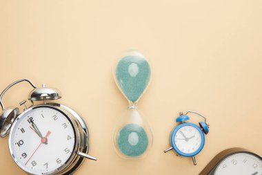 top view of classic alarm clocks and hourglass on beige background clipart