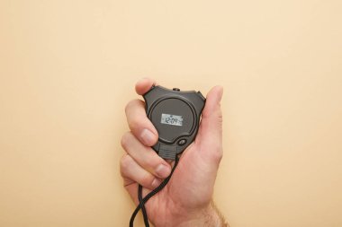 cropped view of man holding stopwatch on beige background clipart