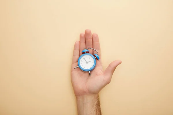 ベージュの背景に小さな目覚まし時計を持つ男のクロップドビュー — ストック写真