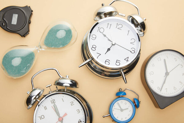 top view of classic alarm clocks, hourglass and stopwatch on beige background