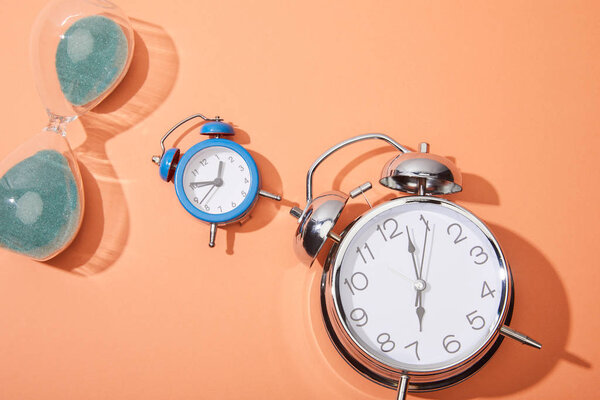 top view of alarm clocks and hourglass on peach background