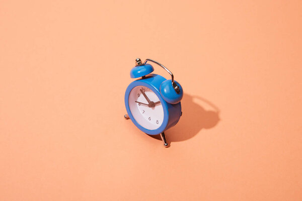 small blue classic alarm clock on peach background