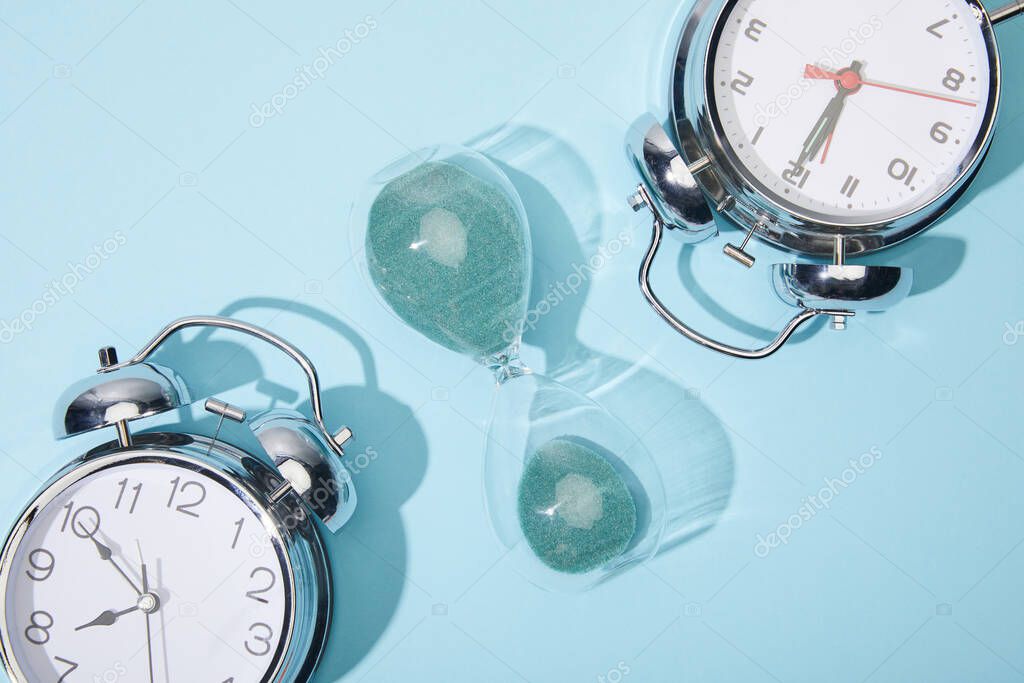 top view of classic alarm clocks and hourglass on blue background