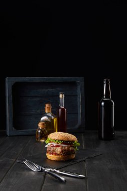 Kara tahta yüzeyde hamburger, çatal, bıçak ve yağ şişeleri siyah üzerine izole edilmiş.