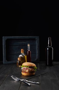 burger on dark wooden surface, fork, knife and oil bottles isolated on black clipart