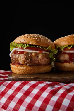 İki hamburger ahşap doğrama tahtasının üzerinde kareli masa örtüsünün üzerinde.