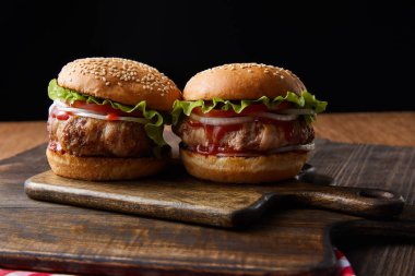 İki lezzetli burger, tahtadan kesme tahtaları siyah üzerine izole edilmiş.