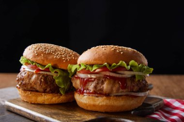 Siyah üzerine izole edilmiş tahta kesme tahtalarında iki hamburger.