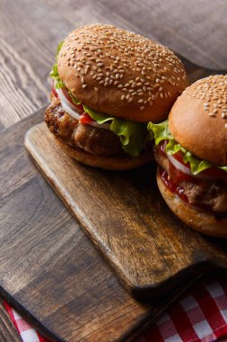 Tahta kesme tahtasındaki iki hamburgerin kareli masa örtüsünün yüksek açılı görüntüsü