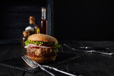 Burgerin seçici odak noktası koyu yüzey, sirke ve yağ şişeleri siyah üzerine izole edilmiş