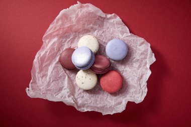 top view of assorted delicious colorful french macaroons on crumpled paper on red background clipart