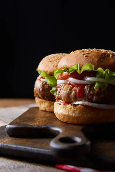 Dois Deliciosos Hambúrgueres Tábuas Corte Madeira Isoladas Preto — Fotografia de Stock