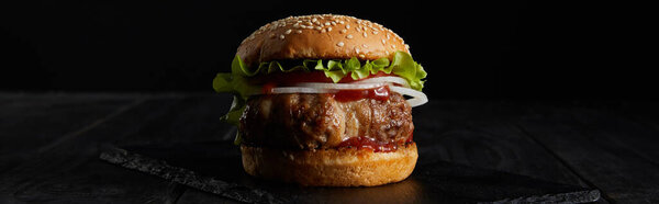 панорамный снимок гамбургера на темной поверхности, изолированный на черной
