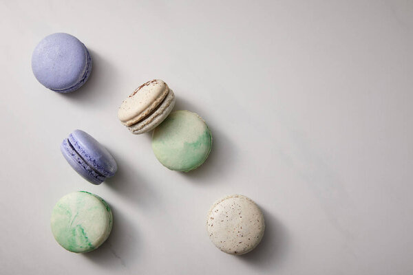 top view of assorted delicious green, violet and white  french macaroons on grey background