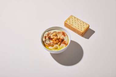 Bowl with delicious hummus near crackers on grey background clipart