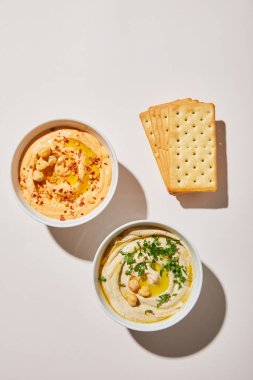 Lezzetli humus ve gri arka planda krakerler olan kaselerin üst görüntüsü.