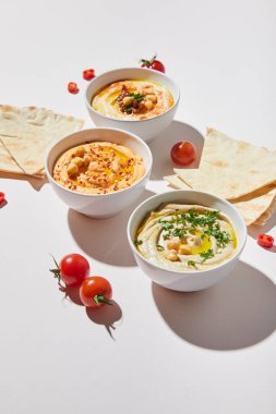 Lezzetli humus, olgun vişneli domates ve gri arka planda pide ekmeği olan kaseler.