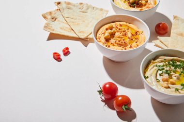 Lezzetli humus, olgun sebzeler ve gri arka planda pide ekmeği olan kaseler.