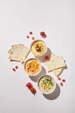 Lezzetli humus, olgun sebzeler ve gri arka planda pide ekmeği olan kaselerin üst görüntüsü.